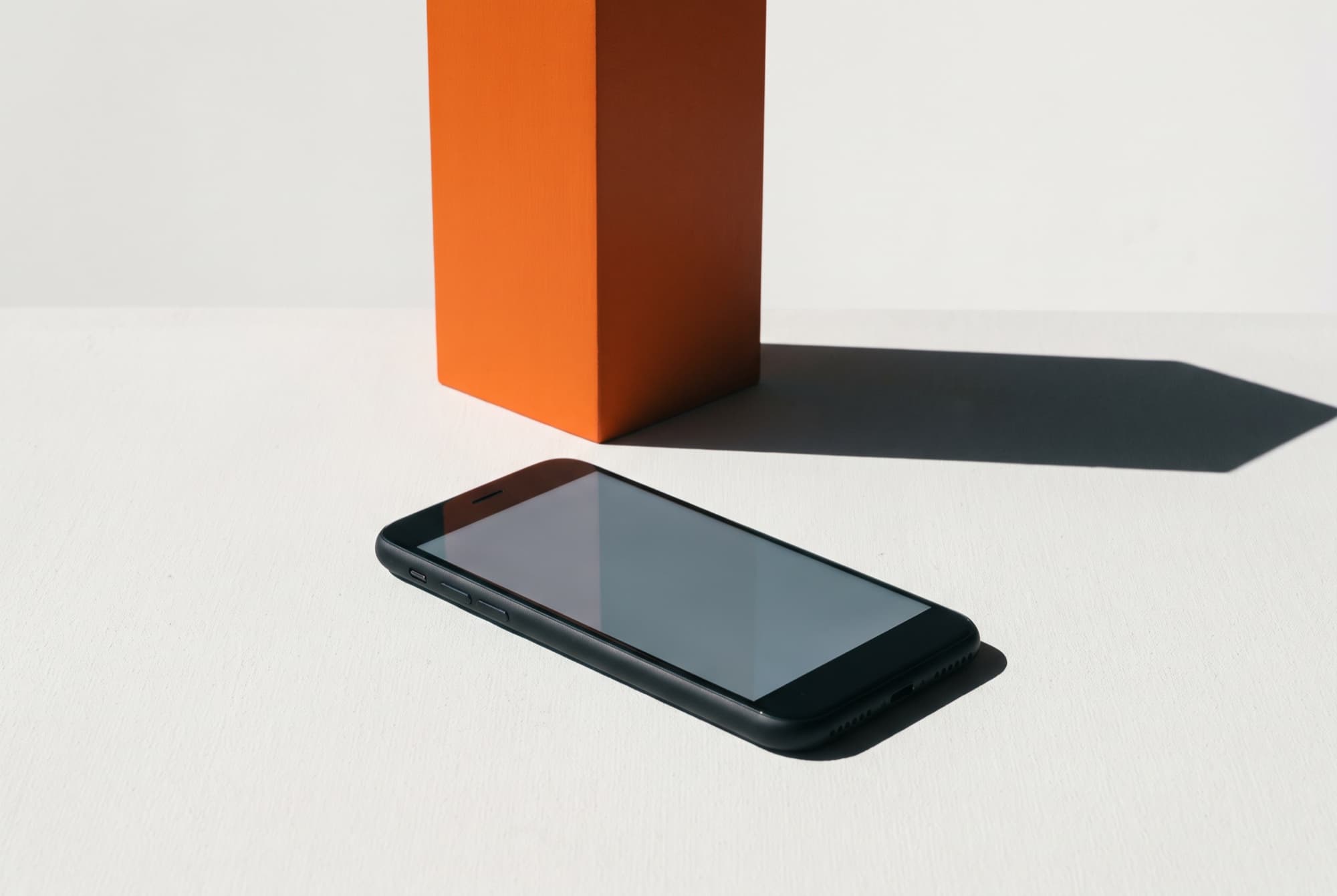 A blank phone lying on a chalk surface with an upright orange panel behind it